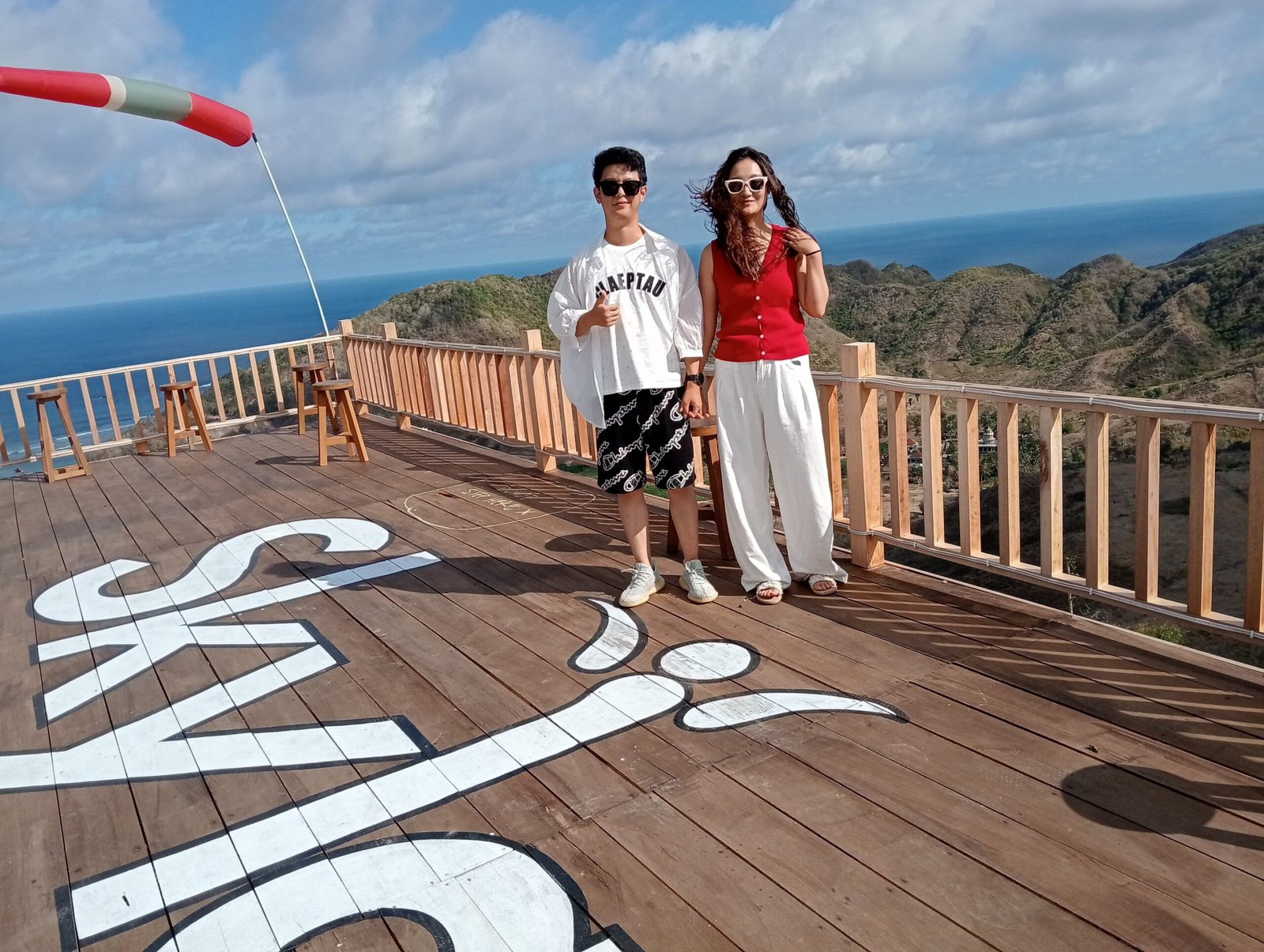 A couple posing on a wooden observation deck with a scenic ocean and mountain view.
